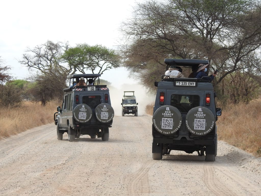 Two Ecolegacy Africa safari vehicles with guests on a dusty park road